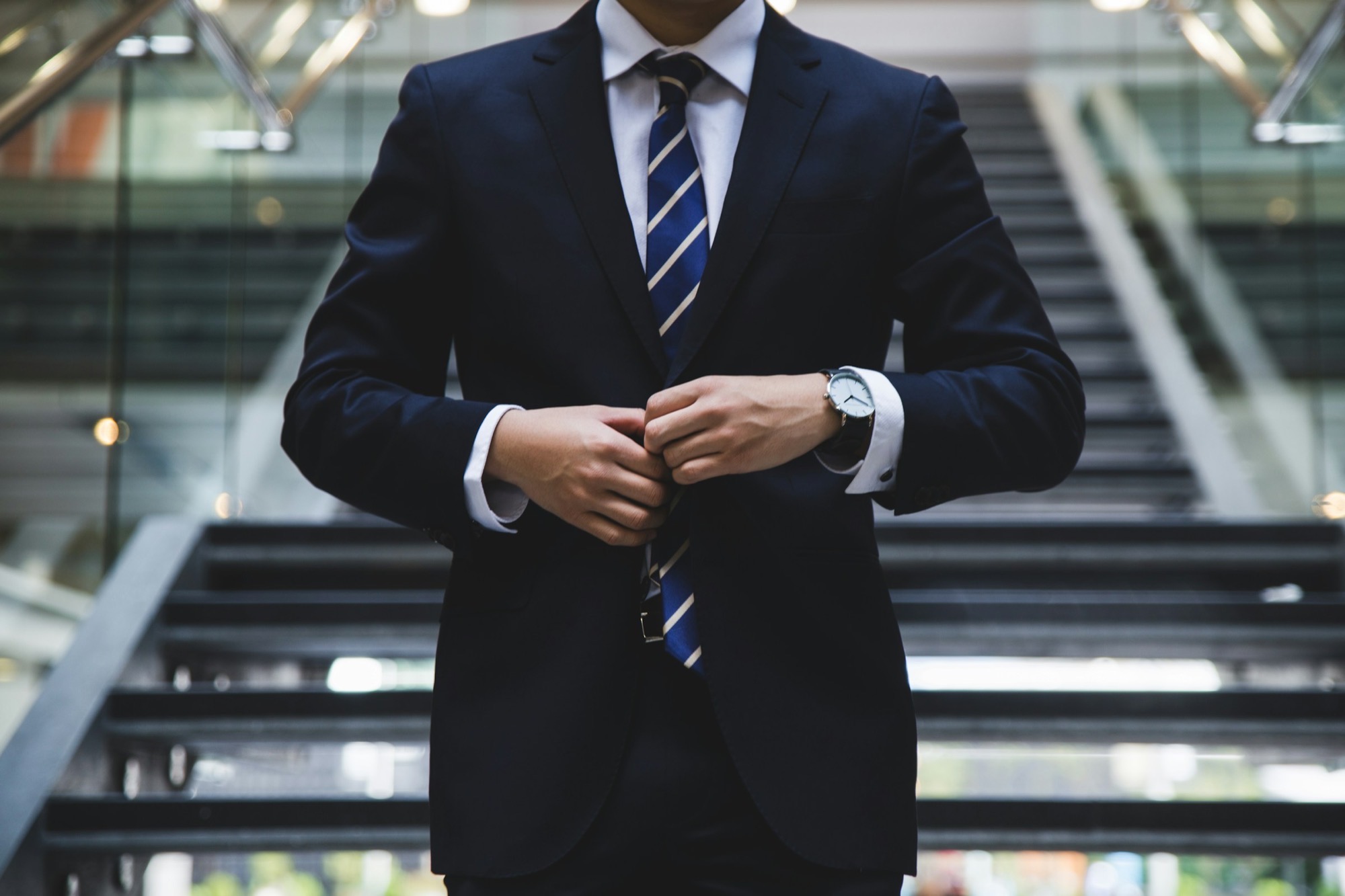 An executive buttoning a suit jacket at the foot of an office staircase